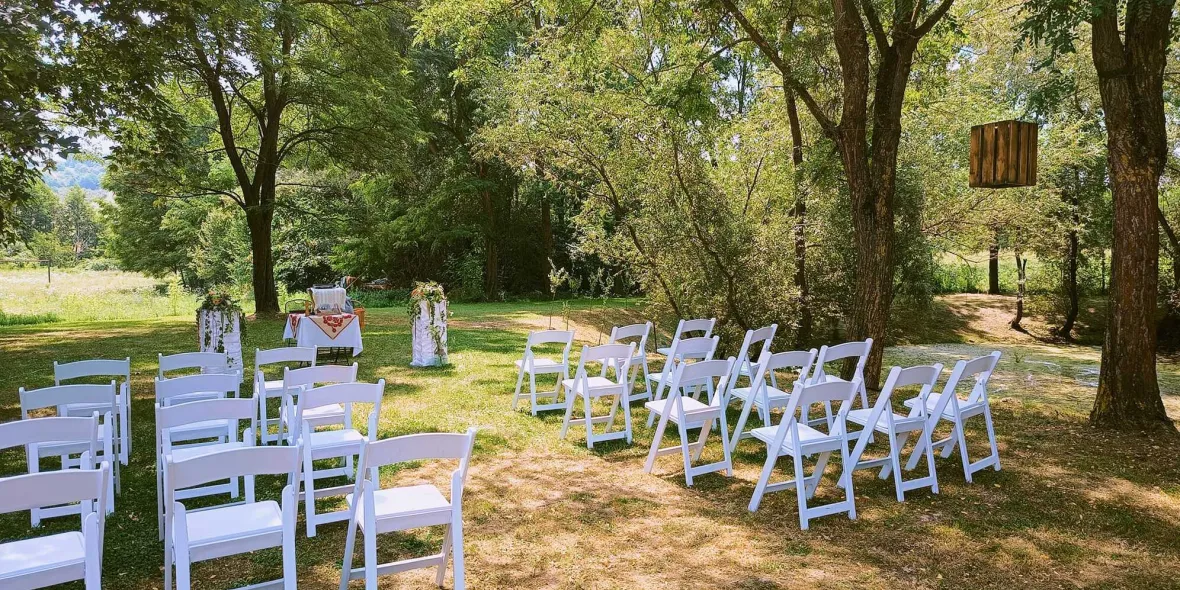 Vedem locatia unei ceremonii in aer liber cu scaune able inchiriate frumos aranjate. În prim-plan se vede o leagăn.