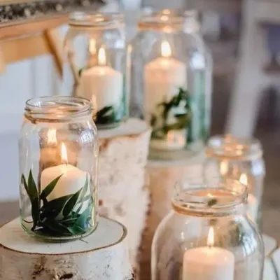 Decor rustic de nuntă în Mureș, cu borcane cu lumânări albe și crengi de brad pe butuci de lemn.