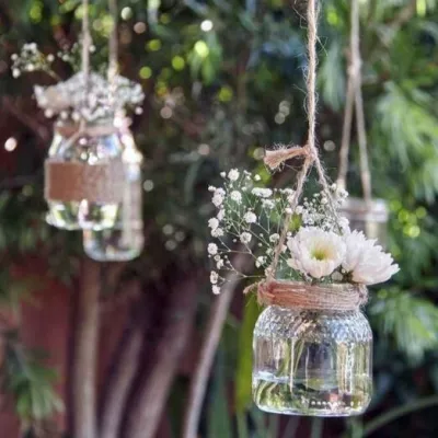 Decor de nuntă rustic în aer liber, cu borcănele simple atârnate, decorate cu sfoară și flori albe.