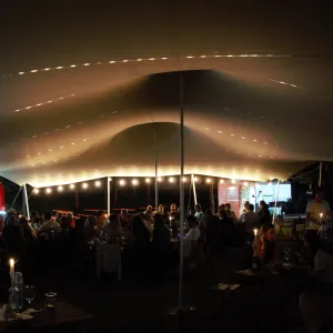 Cort festival de inchiriat, Un cort extensibil închiriat la un festival, oaspeții savurând vin la lumina lumânărilor.