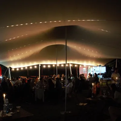 Cort festival de inchiriat, Un cort extensibil închiriat la un festival, oaspeții savurând vin la lumina lumânărilor.