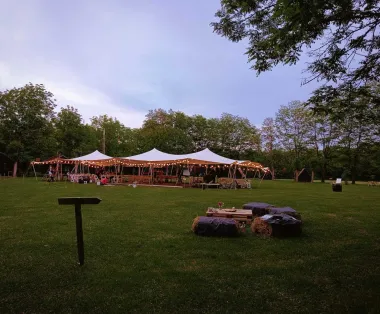 Cort eveniment de inchiriat iluminat, decorat pentru nuntă, cu mese și scaune dedesubt, în aer liber.